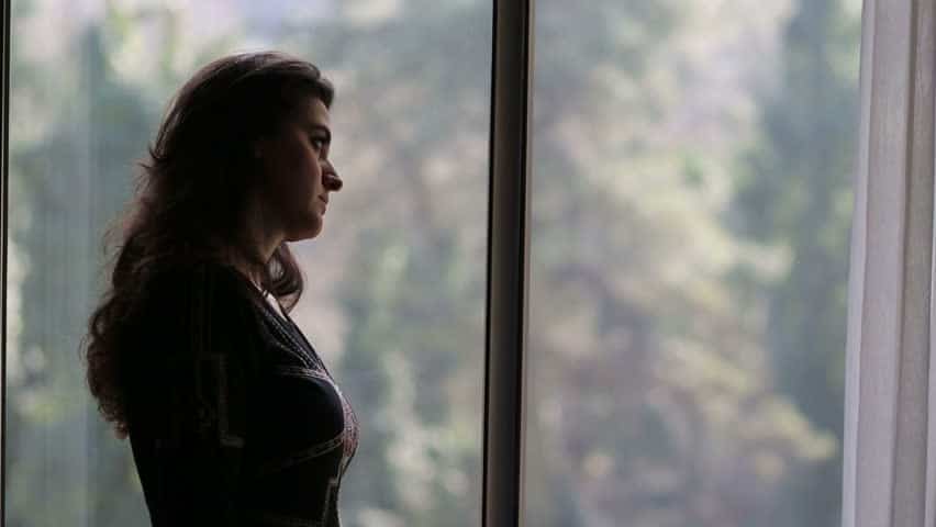 woman leans her head against a window while gazing outside.