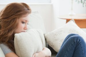 Sad red-haired woman cradles a pillow while sitting on a couch