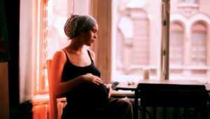 Pregnant mom sits in window nook and thoughtfully looks out the window.