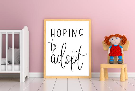 A crib, chair, and doll frame a whiteboard with "Hoping to Adopt" written on it.