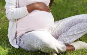Pregnant mom sits cross-legged in the grass while cradling her belly.