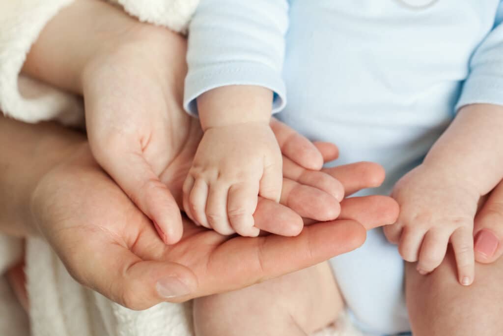 a baby holds a woman's hand which is cradled in a man's hand.
