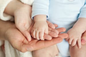 a baby holds a woman's hand which is cradled in a man's hand.