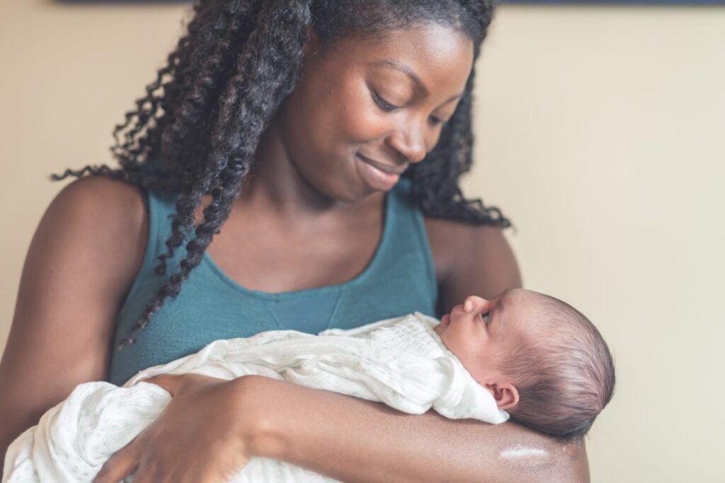 A dark skinned woman cradles a new born child while smiling