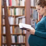 Good mom: Pregnant student reading a book in a library